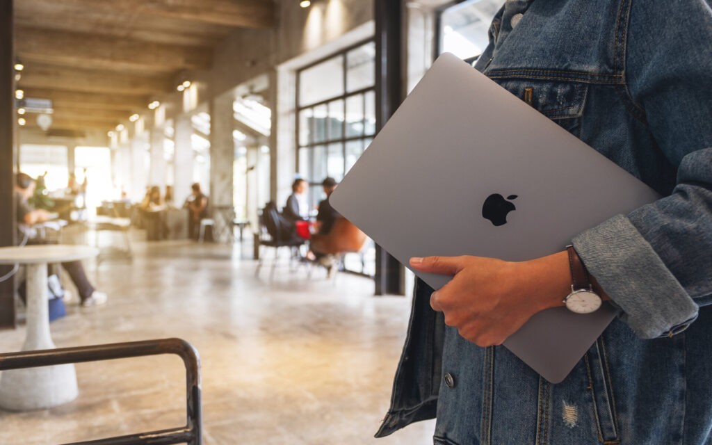 Eine Frau hält ein Macbook Pro in der Hand unter dem Arm