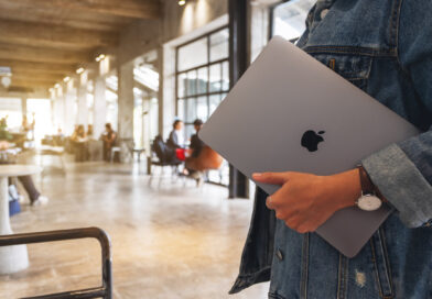 Eine Frau hält ein Macbook Pro in der Hand unter dem Arm