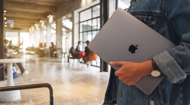 Eine Frau hält ein Macbook Pro in der Hand unter dem Arm